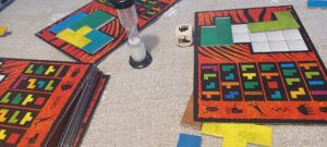 Kuvassa on tiimalasi ja värikkäitä pelilautoja pöydällä.